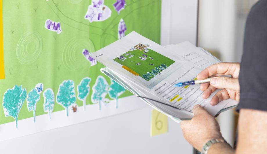 Auf dem Bild sieht man eine Person, welche einen Bewertungsbogen und Stift in der Hand hält und einen Gestaltungsentwurf betrachtet.