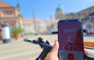 Abgebildet ist eine radfahrende Person, die auf ihr Handy schaut