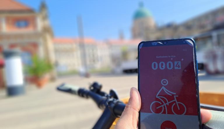 DB Rad+ App Meilenstein Abgebildet ist eine radfahrende Person, die auf ihr Handy schaut